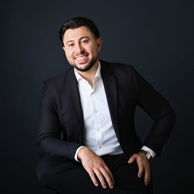 Adan Elias Kornfeld - Founder & Chief Executive Officer Smiling man in a dark suit sitting against a dark background.
